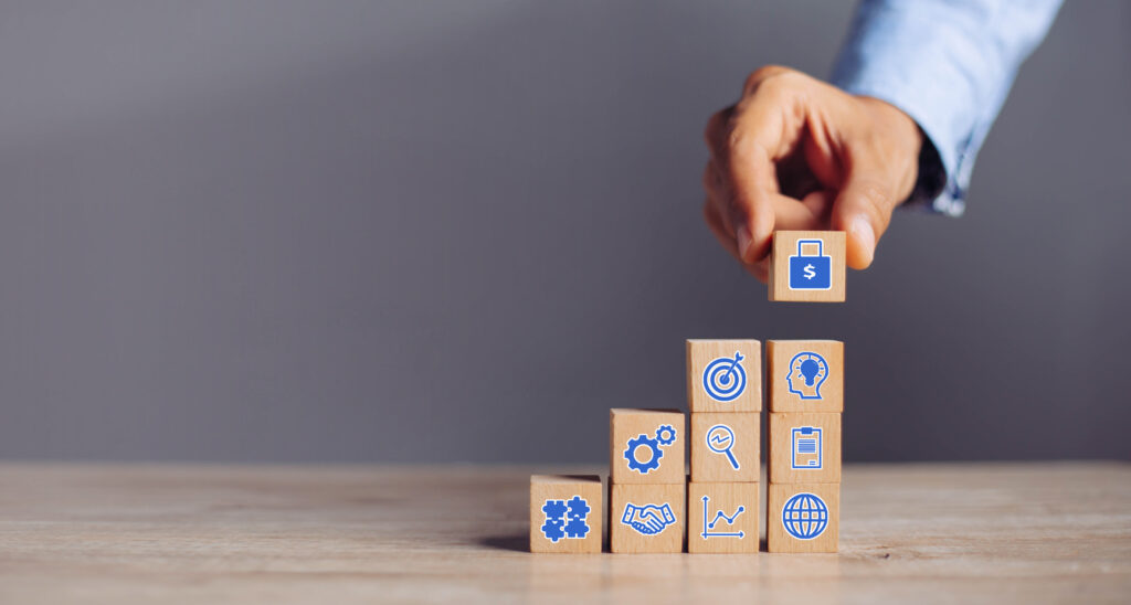 Gestapelde houten blokjes met daarop iconen en een hand die het laatste blokje erop zet